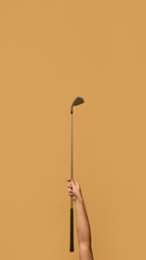Hand gripping golf club, holding it upright against warm brown background, representing balance between control and execution in sport equipment. Concept of sport, energy, control, strategy. Ad