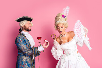 Elegant Royal Themed Couple in Historical Costume Posing Against a Pink Background