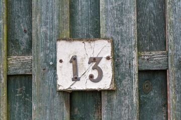 Rusty number 13 and white plate on a rough raw green wooden fence mounted with screws
