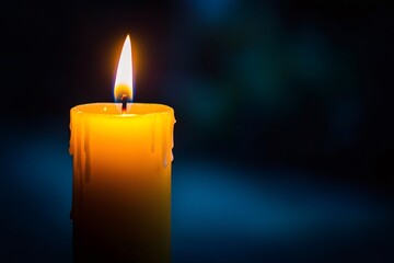 Burning candle illuminating dark background with melted wax