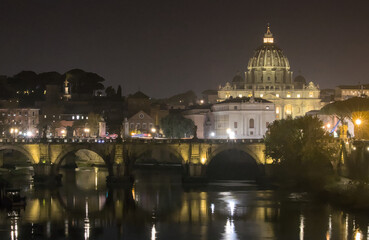 Fototapeta premium A night view of St. Peter's Basilica in the Vatican seen from across the Tiber River. The Ponte Sant'Angelo bridge is visible in the foreground, with its arches and reflections.