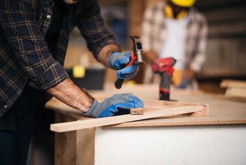 Male craftsman in a workshop environment, carefully measuring and cutting wood, representing...