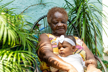Happy black Great-grandmother with her newborn granddaughter on her lap in a natural environment...