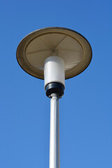 A low-angle shot of a modern street lamp with a round, flat, gray luminaire against a clear blue sky