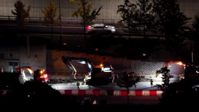 Road construction at night, Excavator(heavy machinery) working on a pile of rubbleon a road, cars passing nearby, constriction site