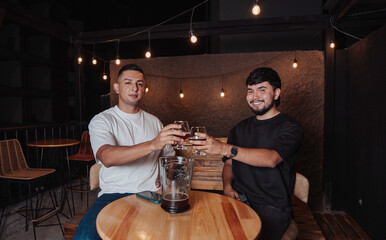 friends clinking their beer glass while smiling for the camera in a bar