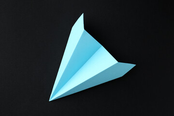 One handmade light blue paper plane on black background, top view