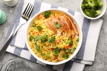 Tasty rice with vegetables and chicken served on grey table, top view