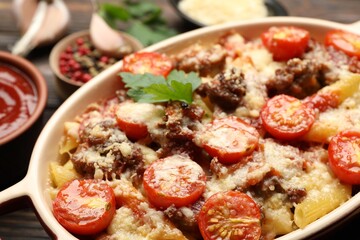 Delicious pasta casserole with cheese, tomatoes and minced meat in baking dish on table, closeup