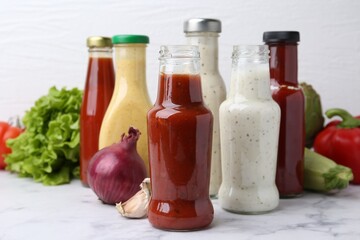 Tasty sauces in glass bottles and fresh products on white marble table, closeup