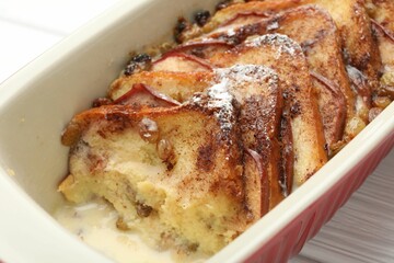 Freshly baked bread pudding in baking dish on white wooden table, closeup