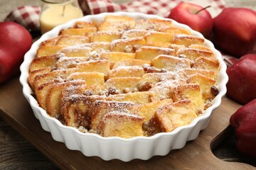 Delicious bread pudding with raisins, powdered sugar and apples on wooden table, closeup