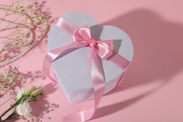 Beautiful wedding gift, pearl jewelry and flowers on pink background, above view