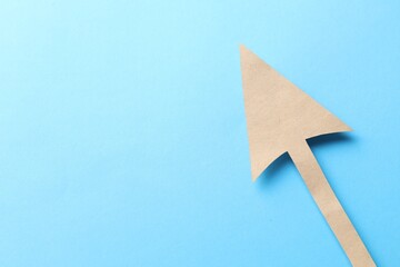 One kraft paper arrow on light blue background, top view. Space for text