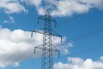 High voltage transmission line and metal framework pylon against sky with clouds