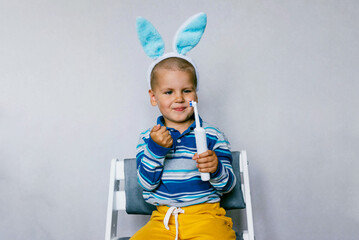 Child boy smiling with toothbrushes in their hands with rabbit ears on a gray background. Medicine, dental hygiene concept. Happy Easter.