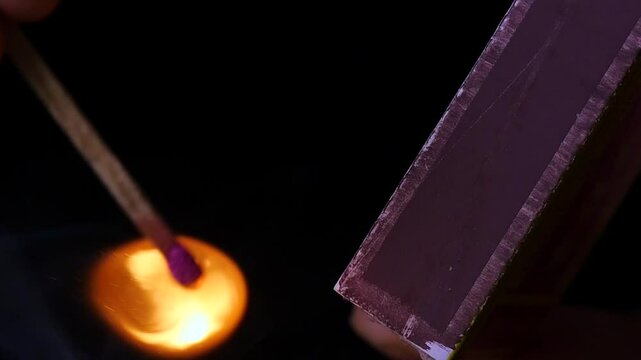 Lighting a match to ignite a tinderbox with careful attention to the flame and the hand's grip