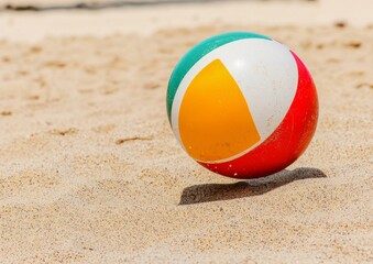 Obraz premium A colorful beach ball rests on the warm sand under the bright sun, inviting fun and relaxation by the seaside.