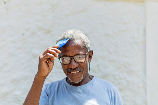 Handsome elderly black man using a blue fork comb in his hair. African man. Senior African. Rio de Janeiro, Brazil.