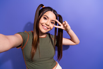 Cheerful young woman posing with peace sign against vibrant purple background
