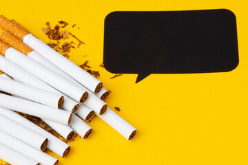Pile of cigarettes on the left side with tobacco all around and black bubble for your text separated on the yellow background.