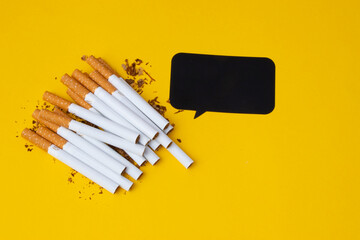 Pile of cigarettes on the left side with tobacco all around and black bubble for your text separated on the yellow background.