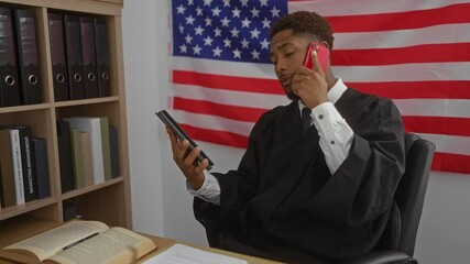 Young man in judge robe holding tablet and talking on phone in office with american flag - Powered by Adobe