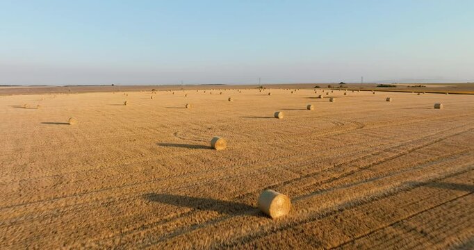 Aerial perspective of straw bales arranged across dry fields, set breathtaking sunset aerial view. Rch textures of cut hay and rolling land form a serene countryside composition.