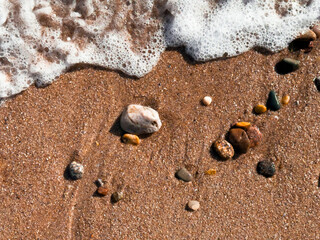 Ocean waves gently lapping on sandy beach with colorful pebbles