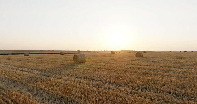 Aerial perspective of straw bales arranged across dry fields, set breathtaking sunset aerial view. Rch textures of cut hay and rolling land form a serene countryside composition.