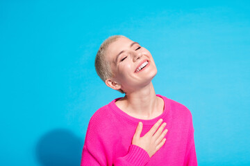 Joyful young woman with short blonde hair wearing a vibrant pink sweater against a lively blue background