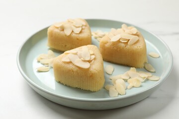 Pieces of delicious semolina halva with almond flakes on white marble table, closeup