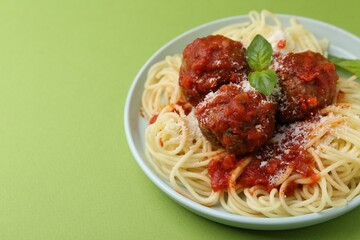 Delicious pasta with meatballs, basil and cheese on green table, closeup. Space for text