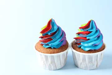 Tasty cupcakes with colorful cream on light blue background, closeup. Space for text