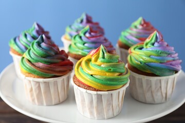Delicious cupcakes with colorful cream on stand against blue background, closeup