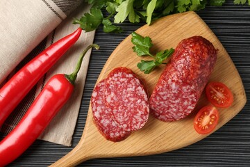 Cut smoked sausage, parsley, tomatoes and chili pepper on black wooden table, flat lay