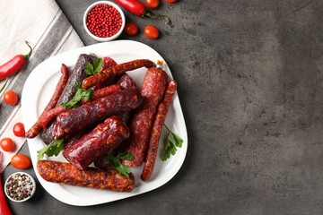 Flat lay composition with different smoked sausages and peppercorns on grey textured table. Space for text