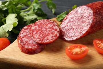 Cut smoked sausage, tomato and parsley on black table, closeup