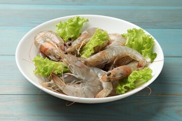Fresh raw shrimps and lettuce on light blue wooden table, closeup