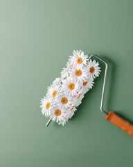 Paint roller covered with white daisies, creating effect of painting with flowers, against green background. Concept of renovation, nature, freshness, creativity.