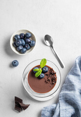 Chocolate pudding in a glass with fresh blueberries and mint on a light background