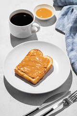 Peanut butter toast on a plate on a light background with a cup of freshly brewed coffee and napkin.