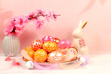 Abstract Easter composition with pink and gold decorated eggs, feathers, flowering branches and flowers. Screen banner with space for greeting text, Happy Easter concept