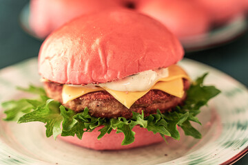Delicious Pink Burger with cheese and fish or beef cutlet with lettuce on a light plate on a dark green background. Close-up.