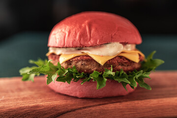 Pink burger with cheese and beef or fish patty with lettuce and sauce on a wooden board and dark background. Close-up. Space for text.