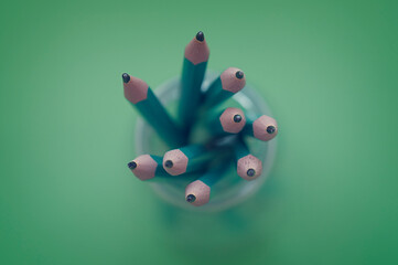 Overhead view of a glass jar filled with green pencils on a green background