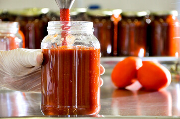 tomato sauce potting process, hands putting tomato sauce in glass jar.