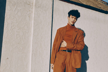 Fototapeta premium Stylish young man in an orange suit against a textured white wall, exuding confidence and contemporary fashion