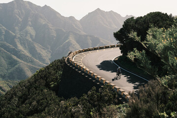 Cyclist on scenic mountain road.  Stunning panoramic view of rolling hills and lush green...
