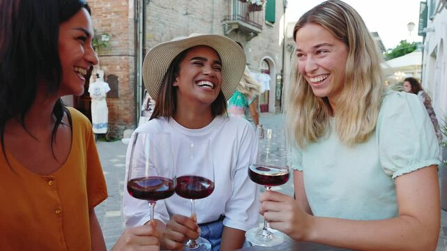 Young happy diverse women friends enjoying time together toasting red wine and eating italian aperitif in a restaurant. Friendship concept.